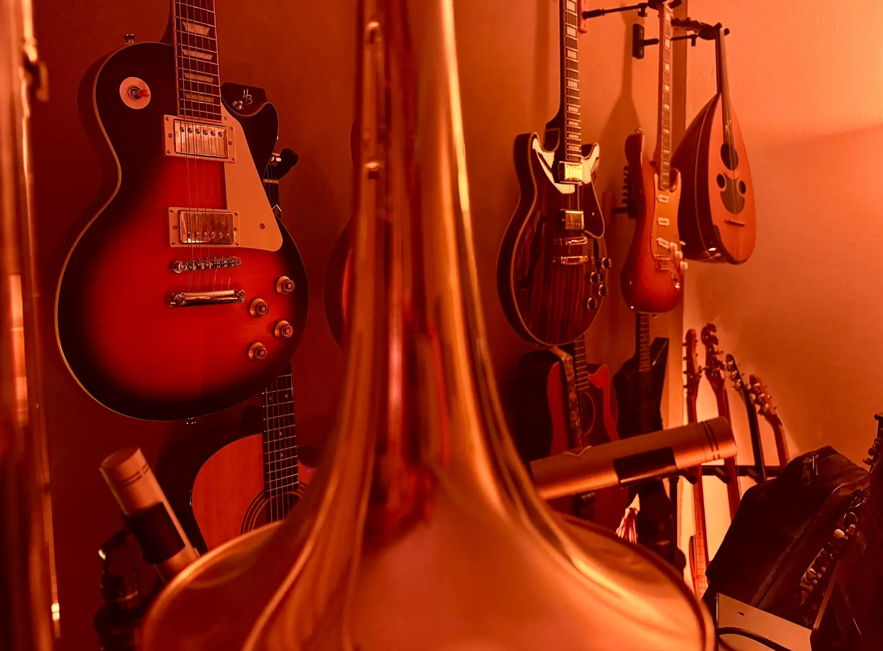 Trombone bell in front of guitars and an oud in red studio light